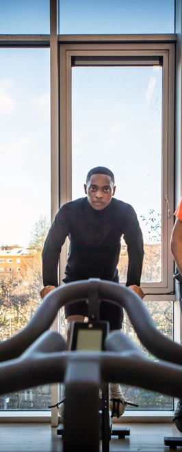 Group of students using exercise bikes in a gym with large windows and a city view. Group of students using exercise bikes in a gym with large windows and a city view.